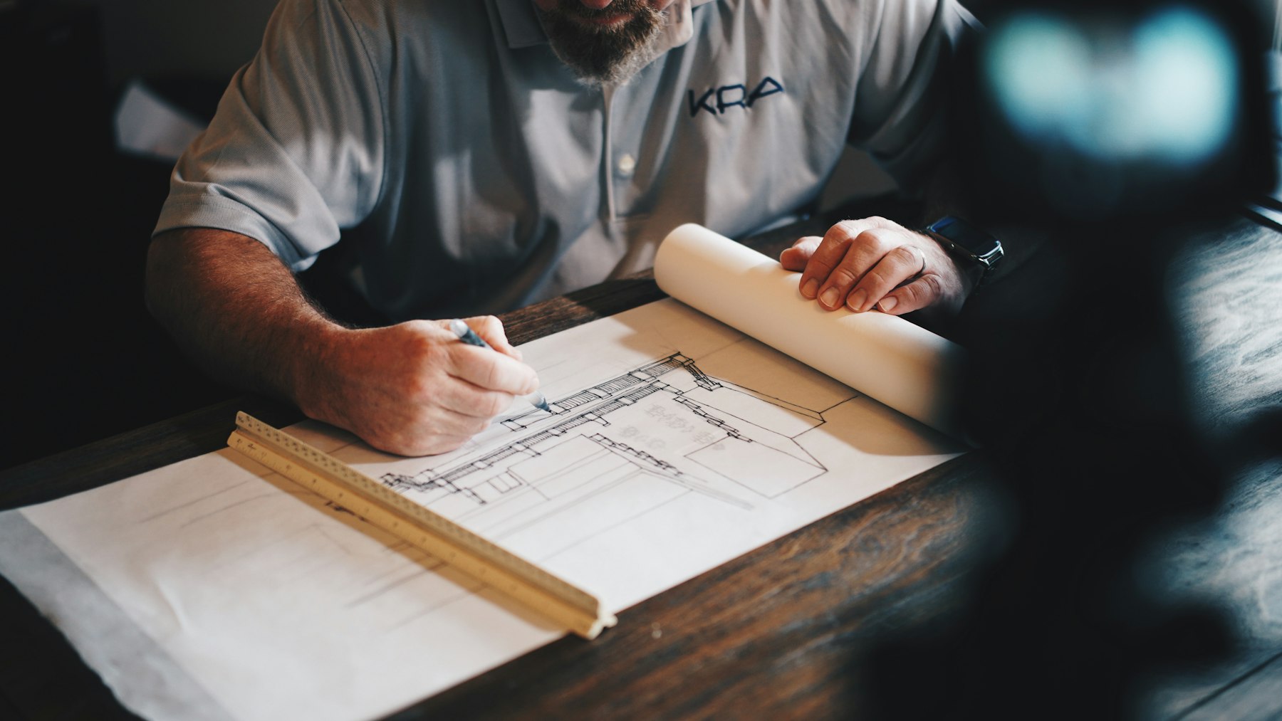 Engineer sketching a building section over technical drawings at a desk