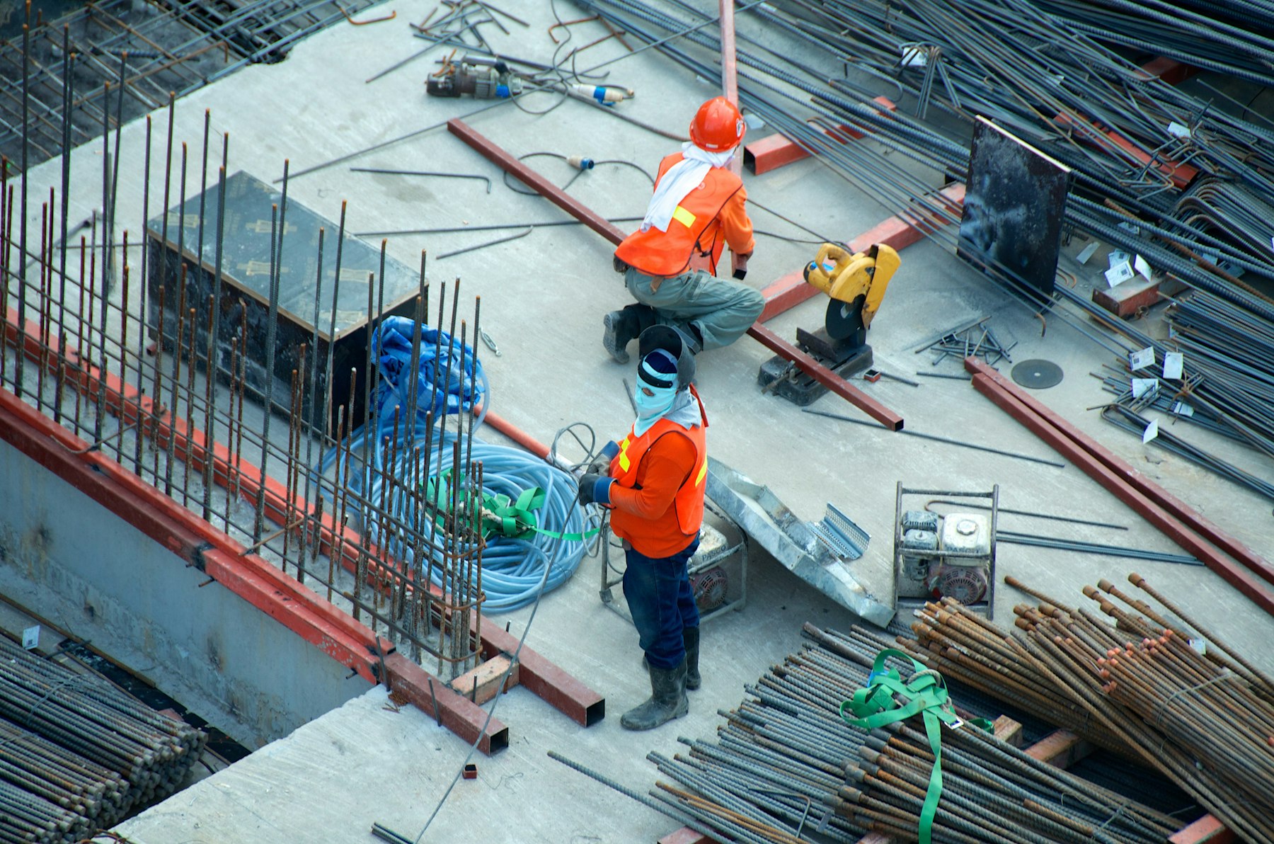 Construction workers laying steel reinforcement bars across a concrete foundation deck