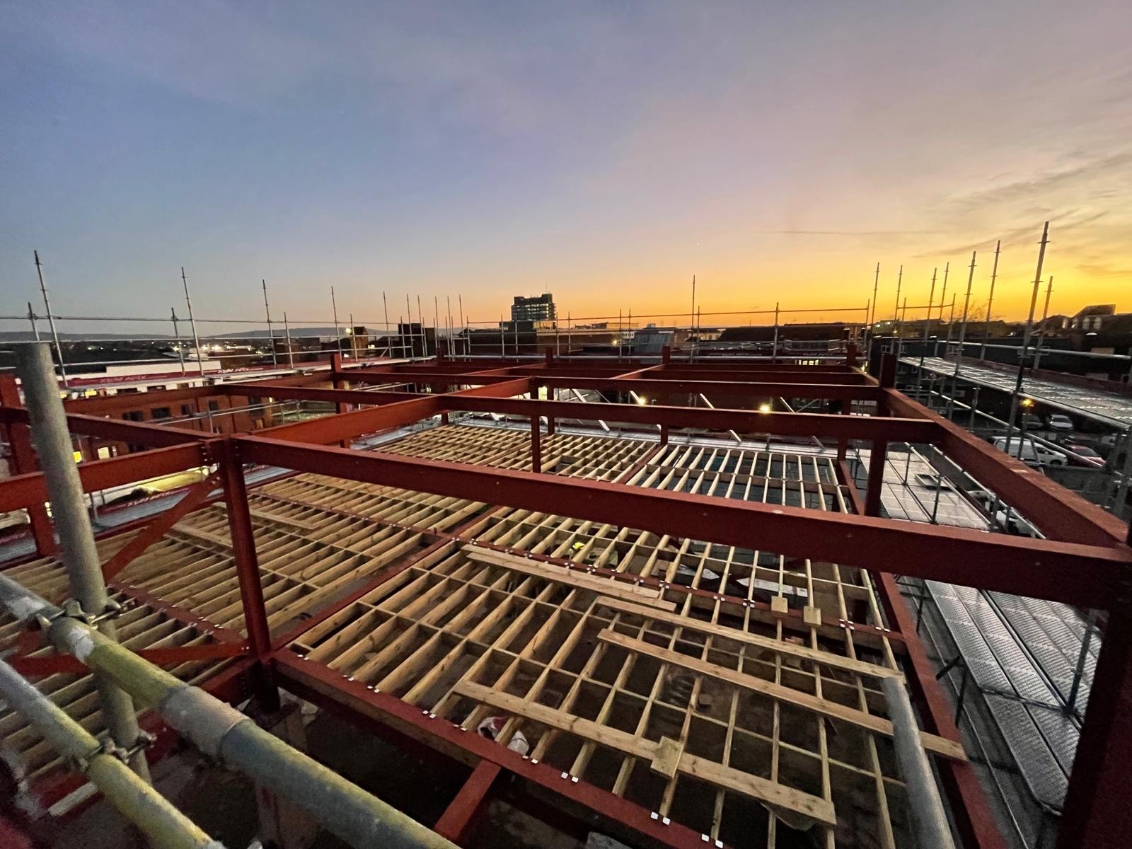 New top-floor steel frame and timber floor joists silhouetted against a dusk sky above Aylesbury